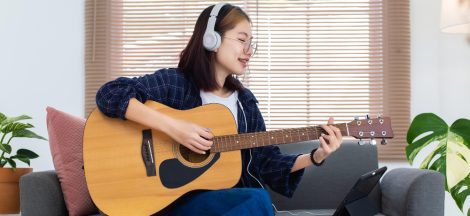 happy-asian-glasses-girl-playing-acoustic-guitar-listening-music-from-tablet-computer-living-room-home-recreation-home-concept